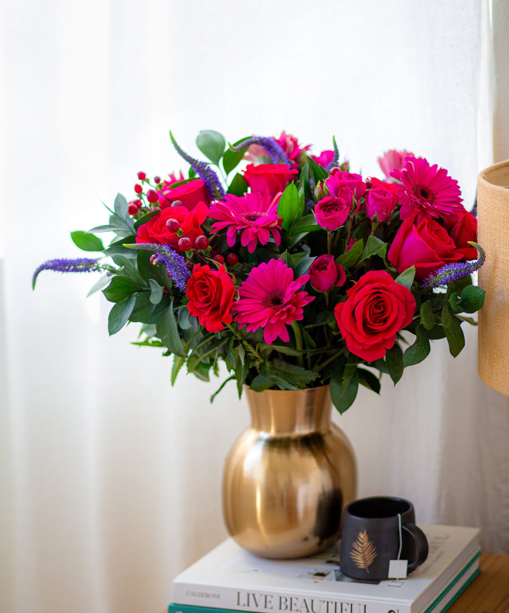 Vibrant floral bouquet featuring pink roses, gerberas, and lush greenery in a gold vase.